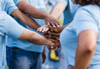 The unrecognizeable group of people stacks their hands in unity.